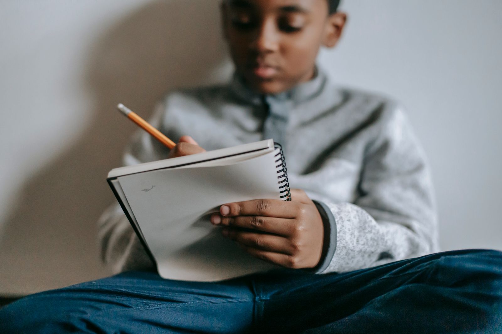 Focused boy writing in a spiral notebook with a pencil