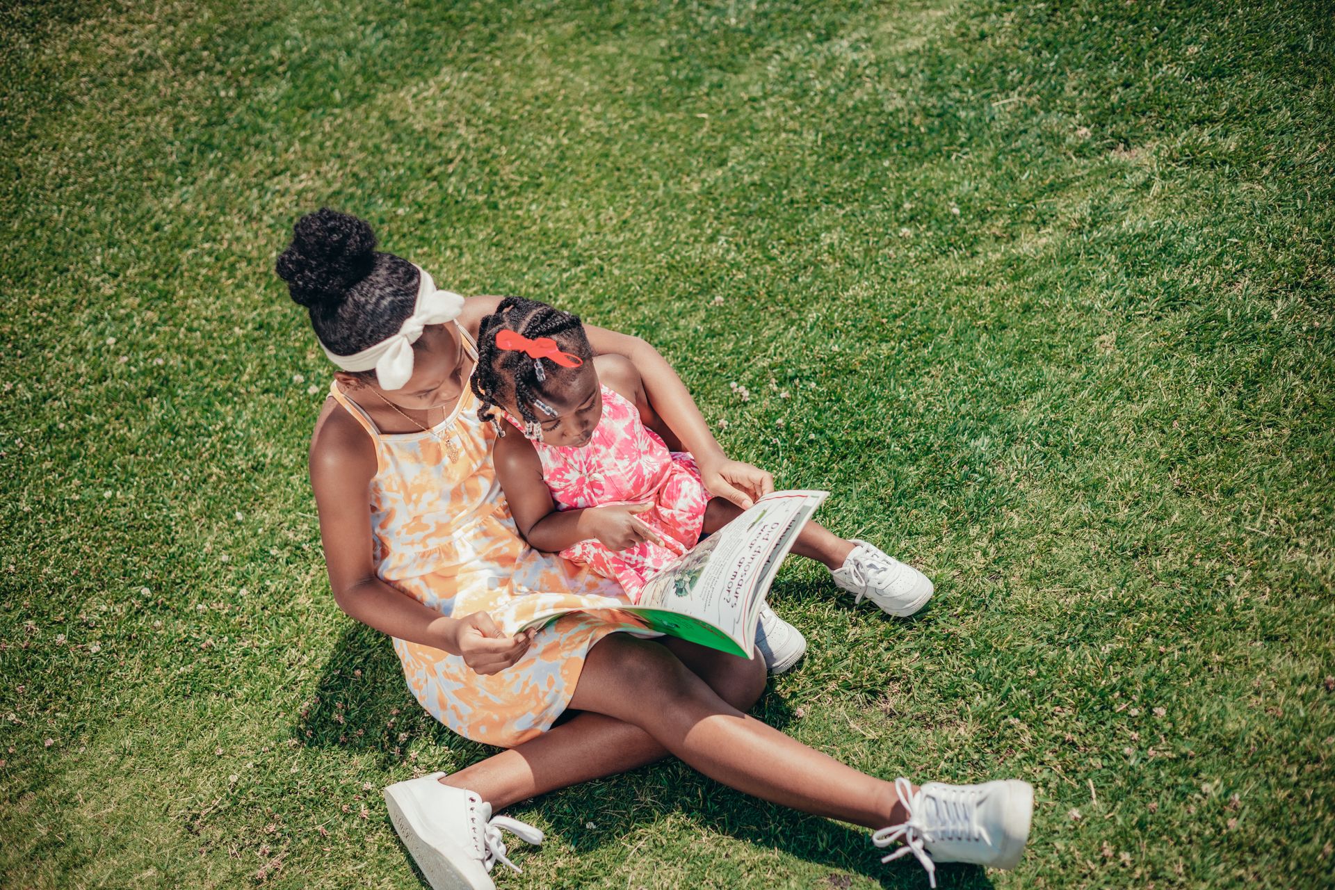 Two girls lying on the grass outdoors reading a book together
