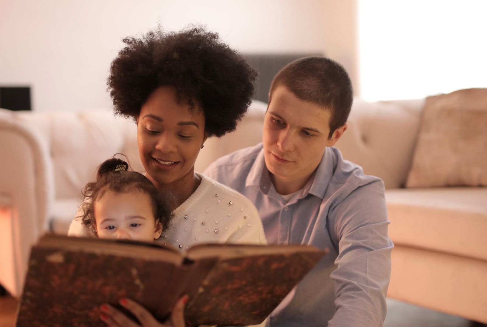 Mother and father sitting on a couch reading a book with their young daughter